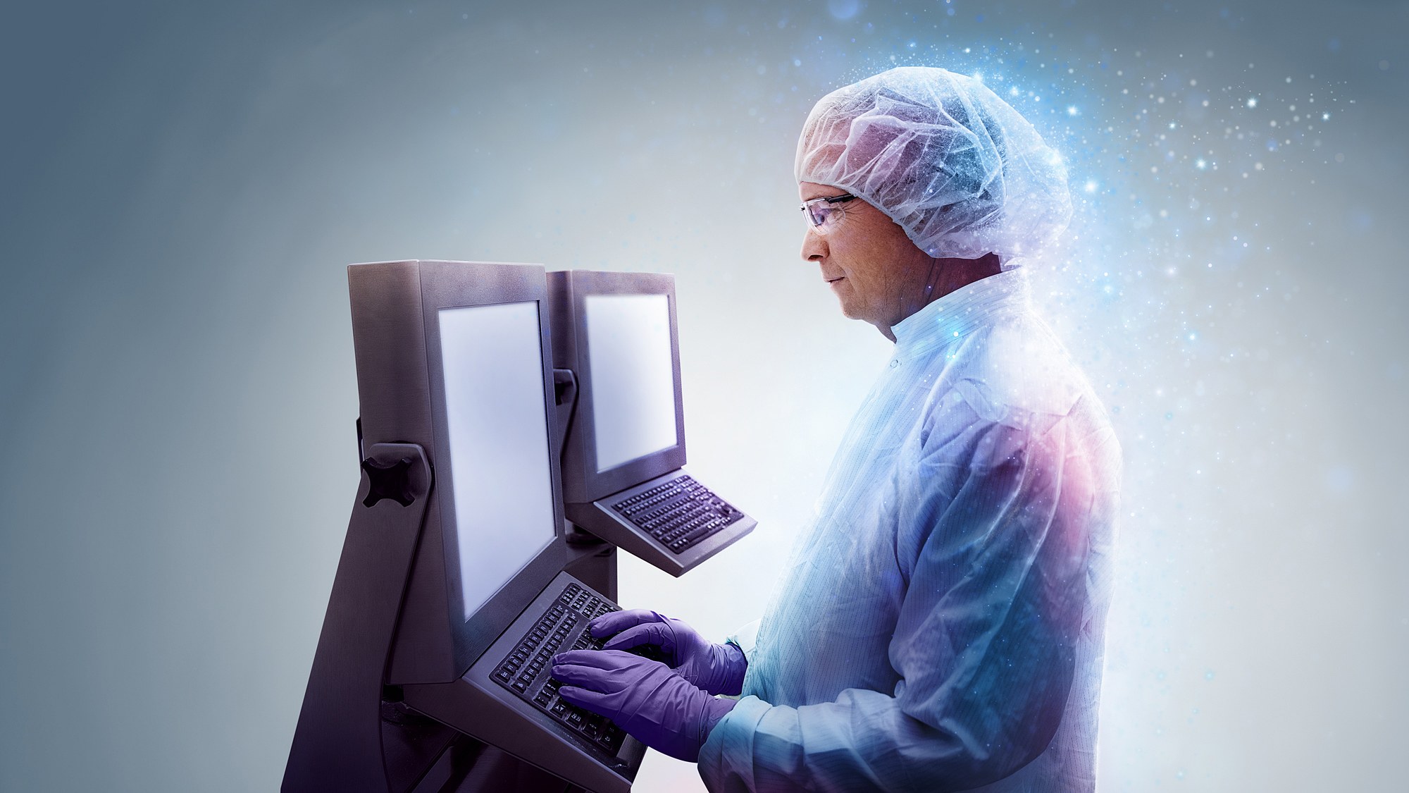 Scientist in cleanroom garments working at a dual-screen terminal