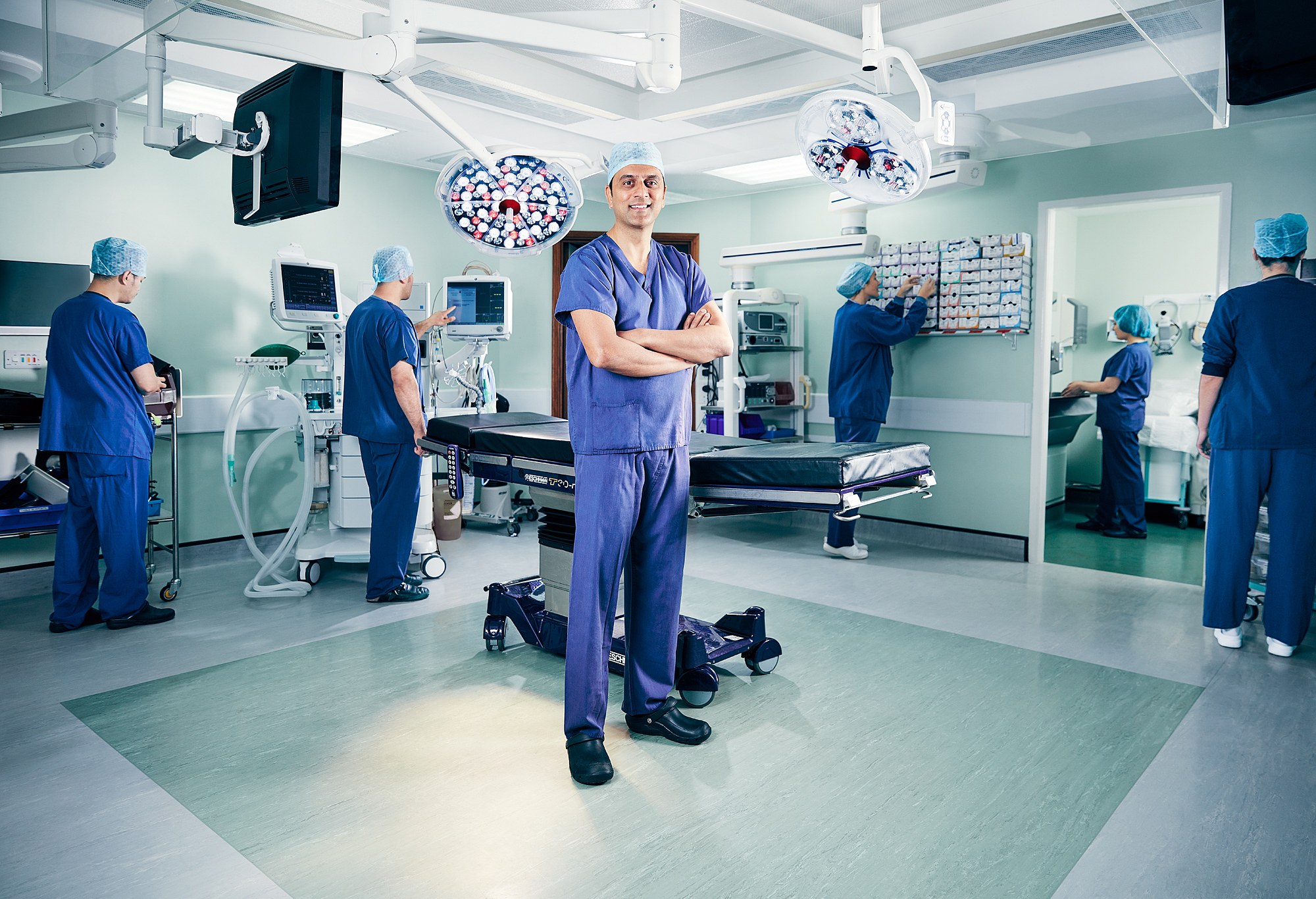 Consultant standing in an operating theatre with the surgical team working around him